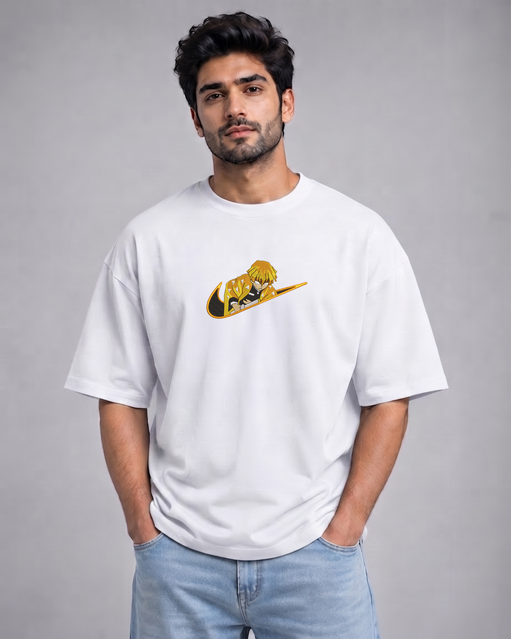 A man wearing a white crewneck t-shirt with a yellow and black graphic print on the chest, paired with light blue jeans, standing against a solid gray studio background.